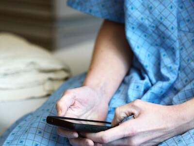 person in hospital gown on mobile phone
