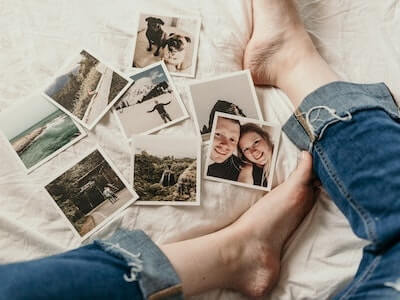 persons feet on bed with polaroid photos of smiling people