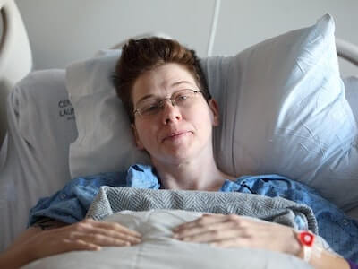 person with short hair in hospital bed looking sad and tired
