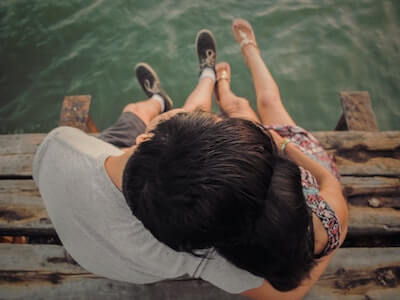 couple sitting on a jetty. They are hugging and resting their heads together. The view is from above.