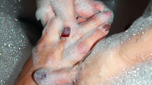 one person washing another persons hands in sudsy water