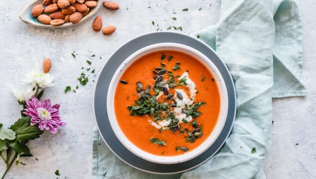 Red orange soup with linen napkins and almonds scattered about.
