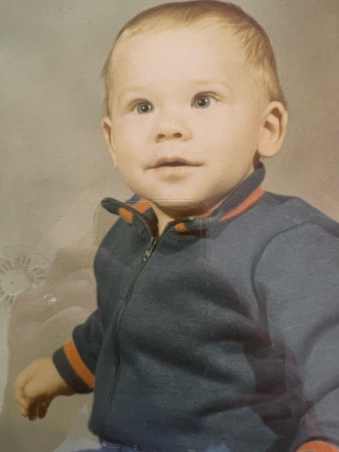 Ian, a baby, sits wearing a blue top