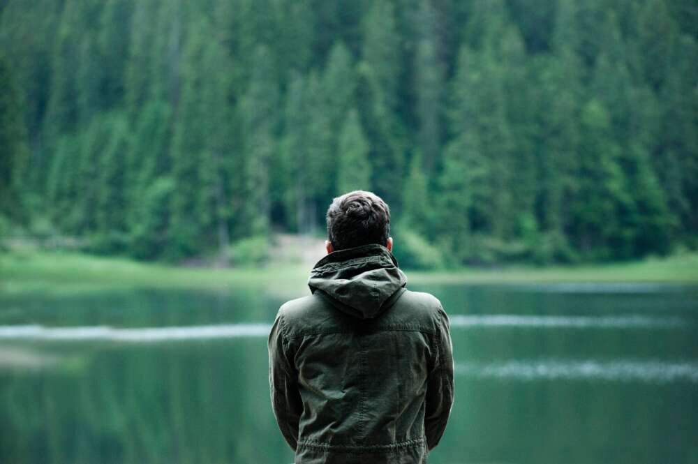 A solo man looks across a body of water in a moment of loneliness.