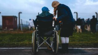 Elderly person in wheelchair is at a park with their carer