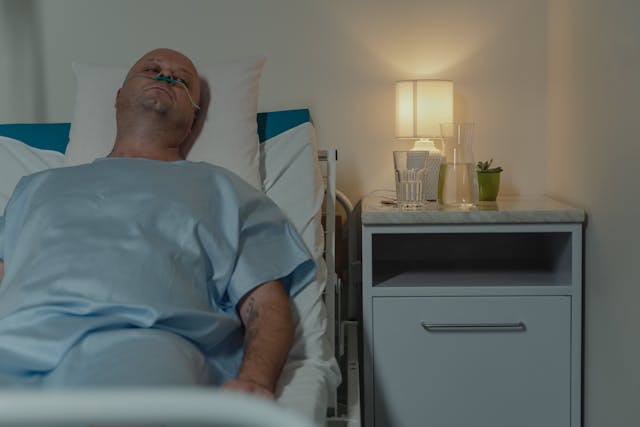A man lays in a hospital bed. He is sad and tired.