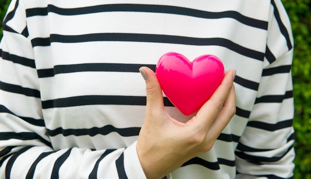 A woman wearing a striped top holds a toy heart in front of her chest