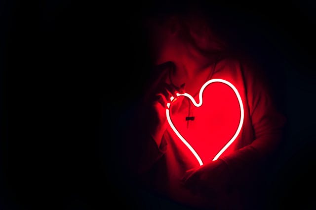 A person holds a neon heart in the dark. It glows red